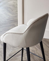 Elegant light beige upholstered dining chair with a smooth, curvilinear backrest and a comfortably padded seat. The chair stands on four slender, matte black metal legs, creating a contemporary and sleek silhouette.