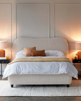 Cozy bed with a curved upholstered headboard, decorative pillows, soft throw, and elegant bedside tables with lamps.