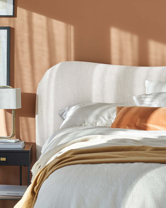 Cozy bed with a textured white headboard, soft linens, and a stylish black nightstand topped with a lamp and decor.