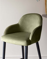 Stylish green velvet chair with curved back and arms, resting on sleek black legs, perfect for modern interiors.