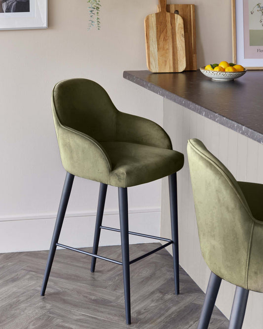 Stylish olive green upholstered barstool with curved back and sleek black legs, complementing a modern kitchen setting.