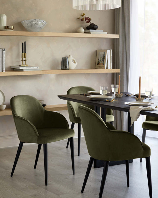 Stylish green velvet chairs with black legs around a modern dark wood dining table; minimal decor on wooden shelves above.