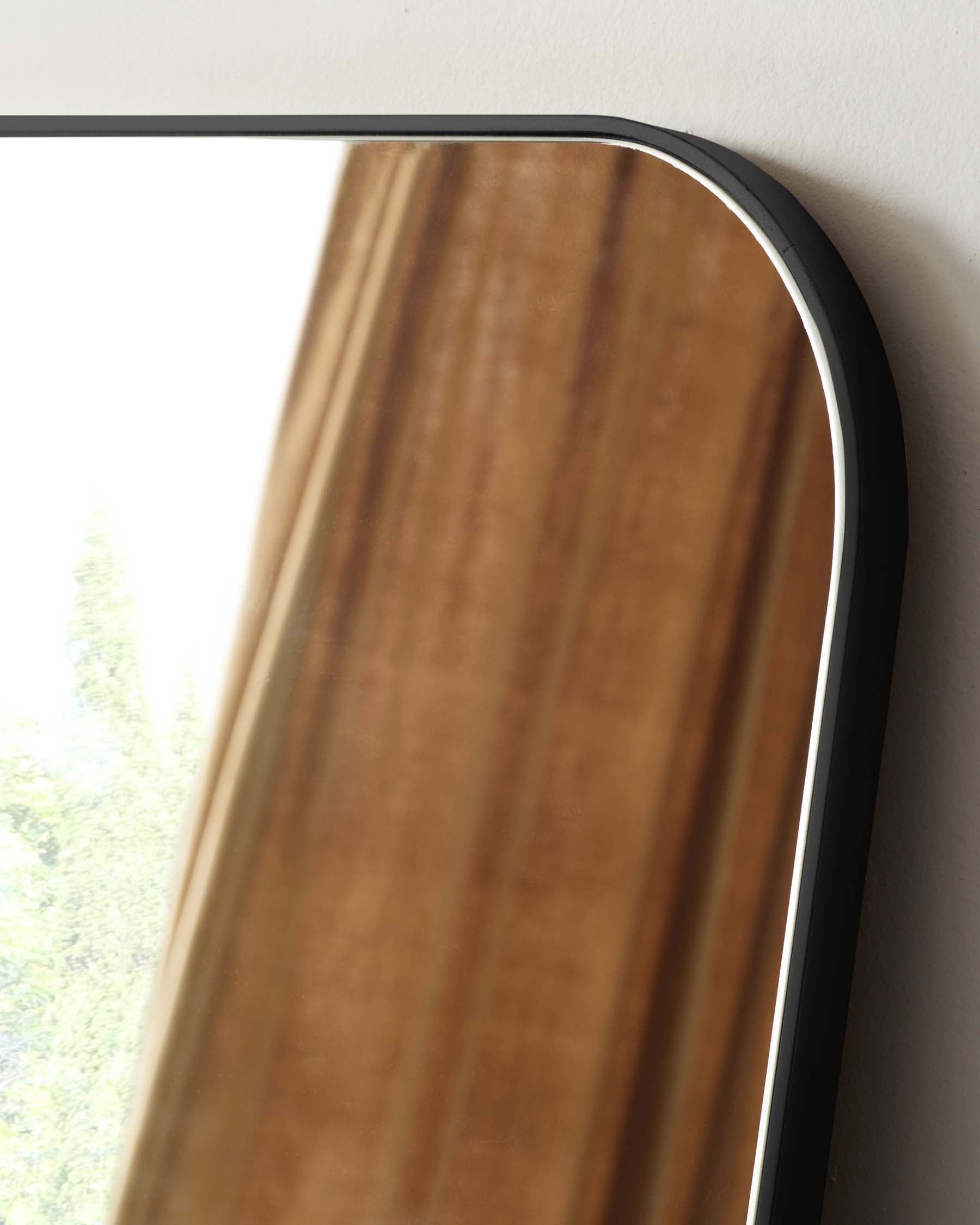 Elegant curved wooden shelf with a sleek black metal frame, mounted against a white wall near a window with a view of green foliage.