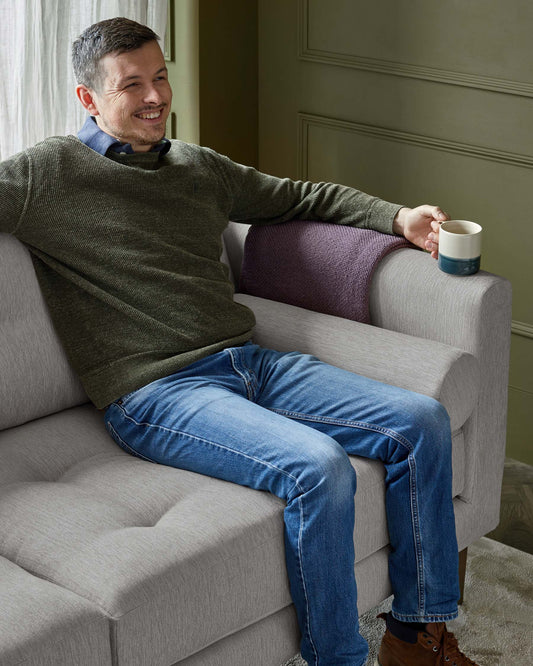 Modern gray fabric sofa with tufted design, complemented by a cozy purple throw. Perfect for casual relaxation.