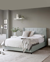 Contemporary bedroom furniture featuring an upholstered queen-size platform bed with a high, tufted headboard in a soft pastel green; matching white bedside tables with a minimalist, modern design; a sleek, white floating wall shelf above the bed displaying decorative items; and a sparse white floor lamp. The ensemble is complemented by soft, neutral bedding and throw blanket, creating a serene and sophisticated space.