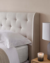 Elegant upholstered headboard with tufted detailing in a neutral beige fabric, complemented by a simple wooden bedside table with a natural finish on display.