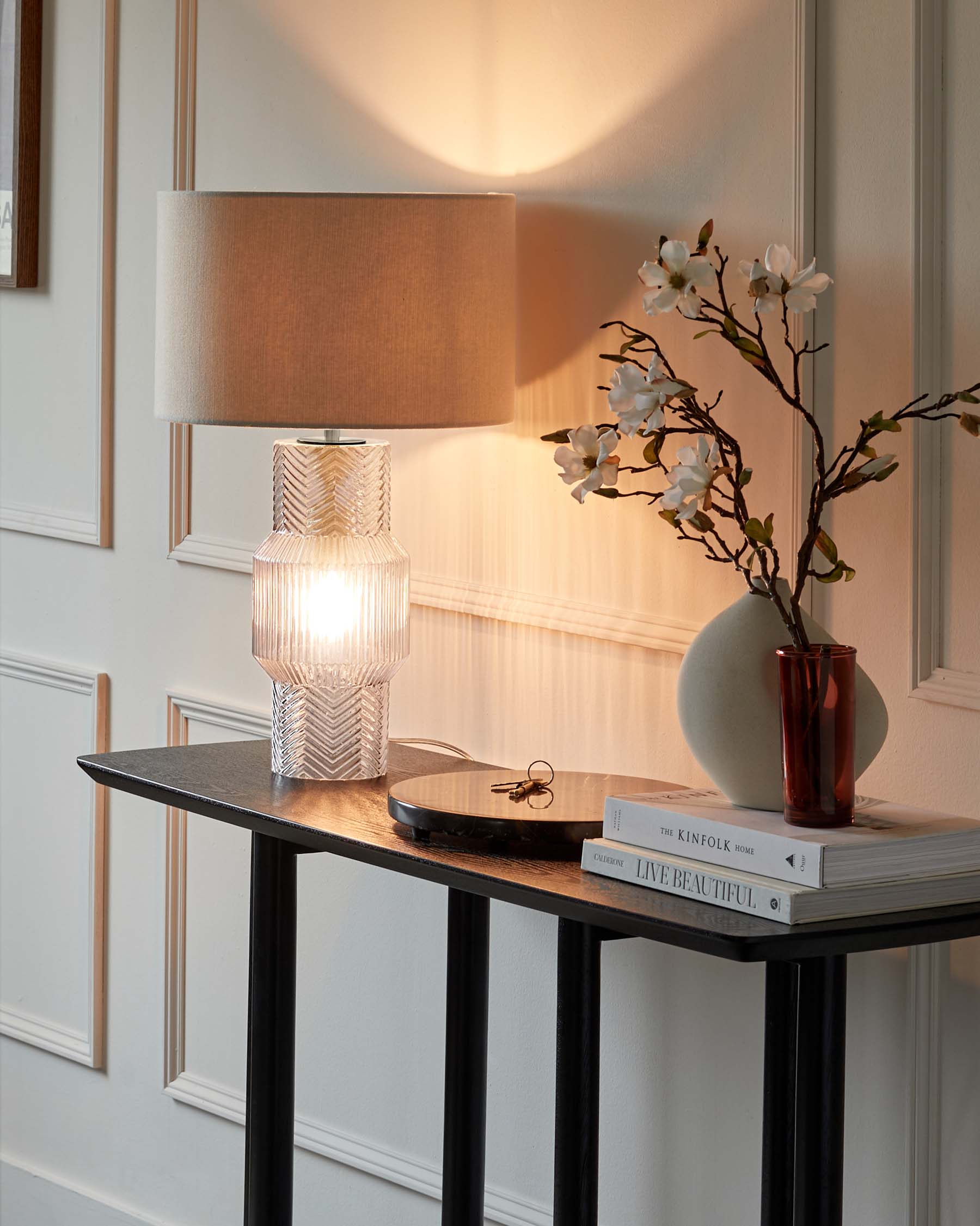 A stylish console table with a textured lamp, a decorative vase, books, and a small round tray with keys.