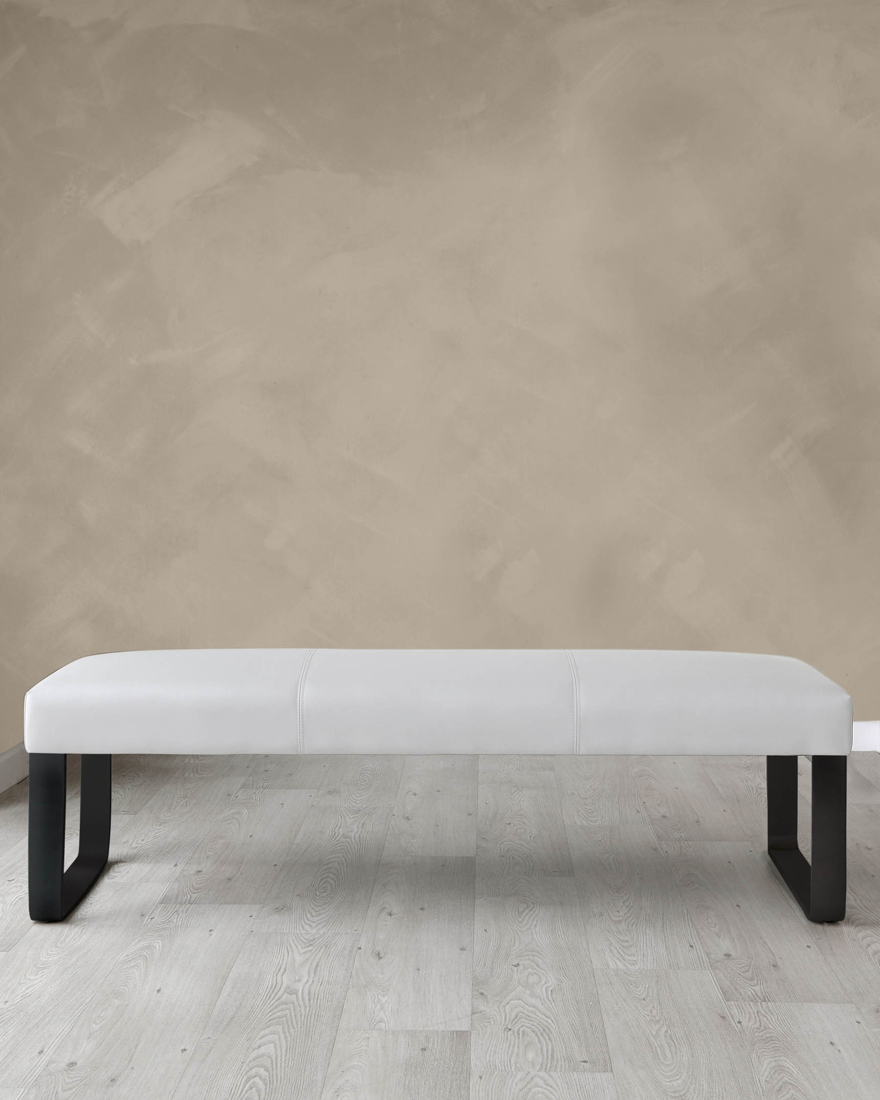 Modern minimalist white upholstered bench with black legs on a light wooden floor against a textured beige wall.