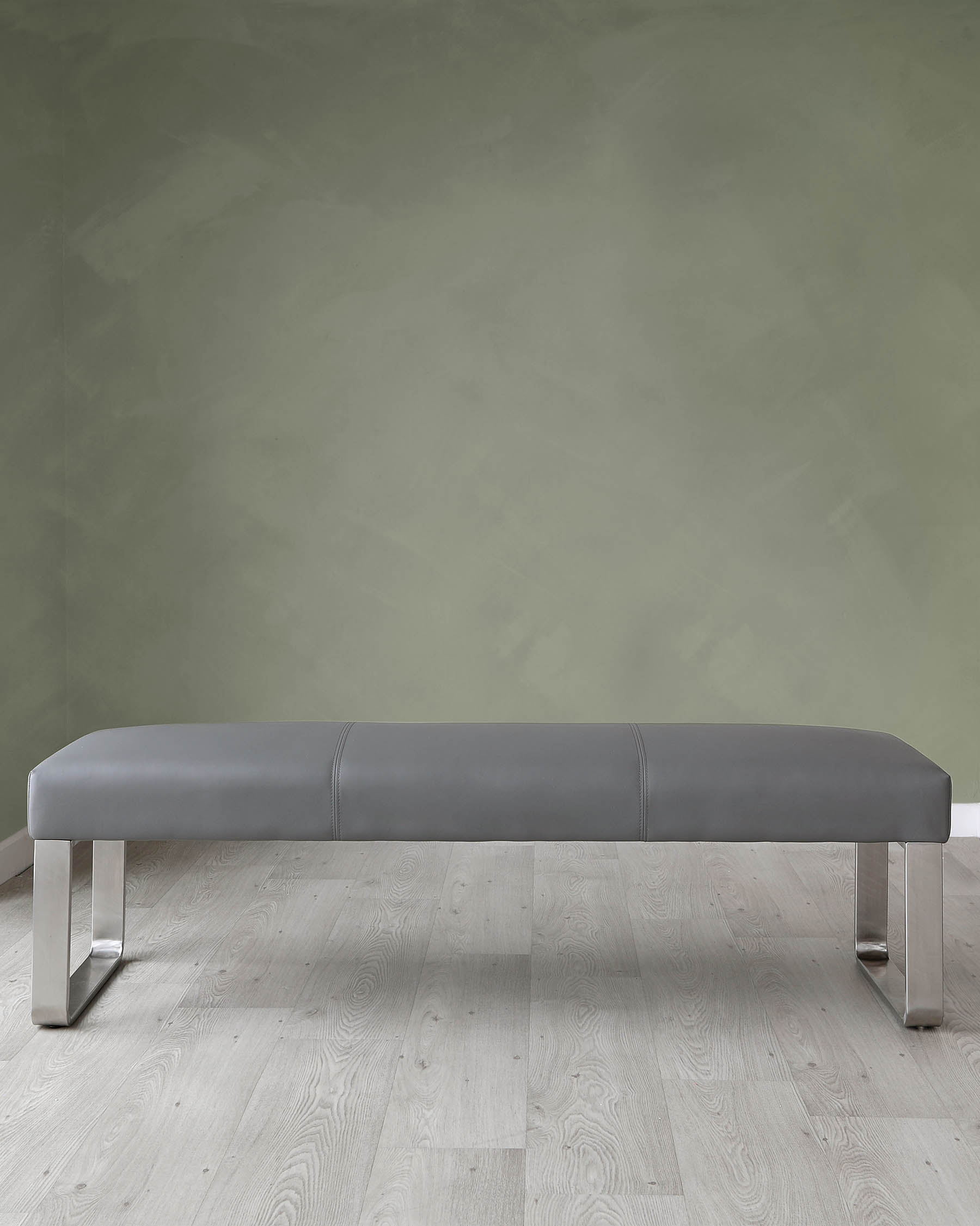 Contemporary grey leather bench with a streamlined design and metallic U-shaped legs on a light hardwood floor against a textured green wall.