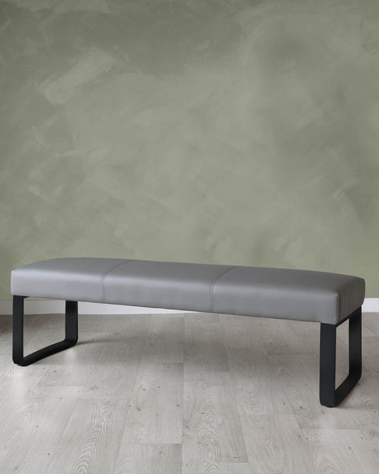 Modern grey upholstered bench with black metal legs on a light wood floor against a textured green wall.