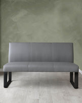 Modern grey upholstered bench with a minimalist design and black legs, positioned against a green textured wall on a light hardwood floor.