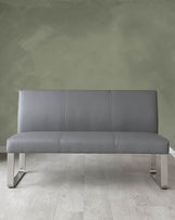 Modern grey leather sofa with a minimalist design and metallic legs on a light wooden floor against a textured green wall.