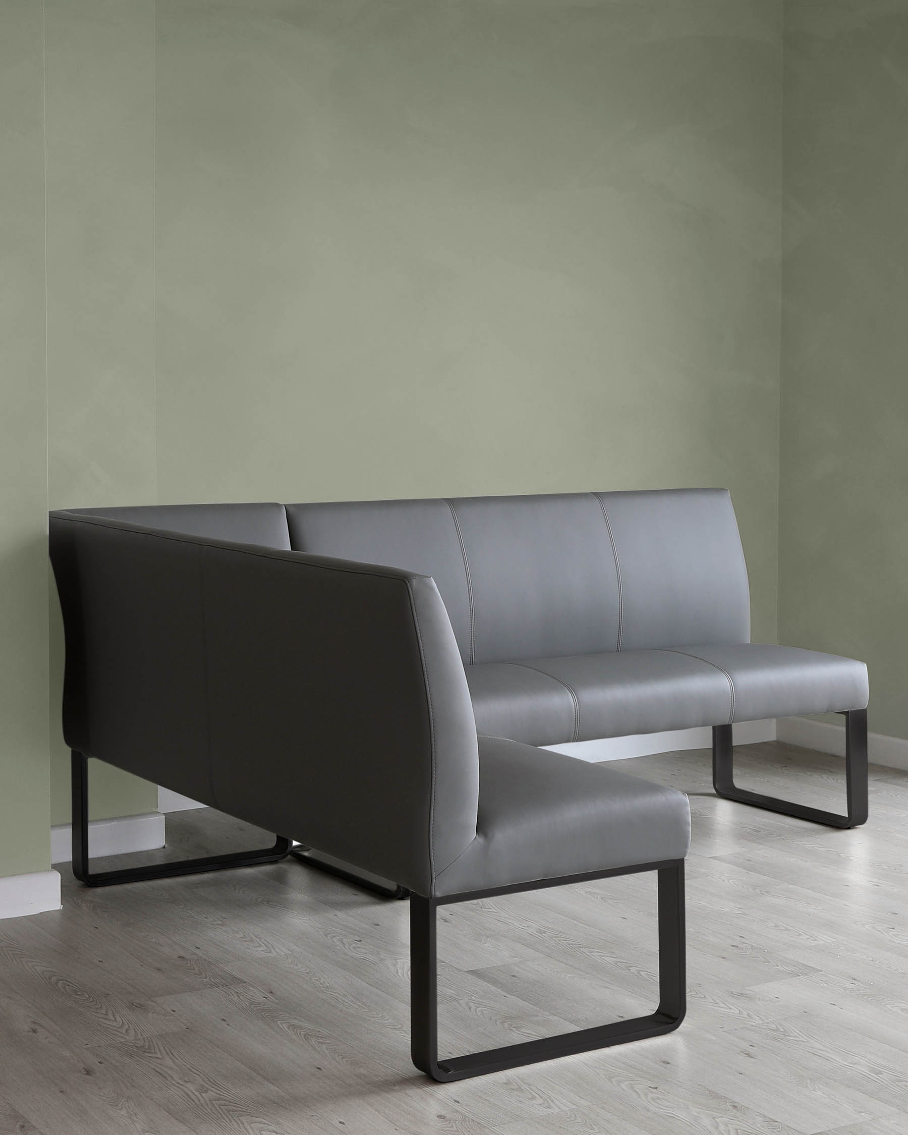 Modern minimalist style dark grey leather bench with a streamlined silhouette and angular matte black metal legs, positioned against a muted green wall over light wood flooring.