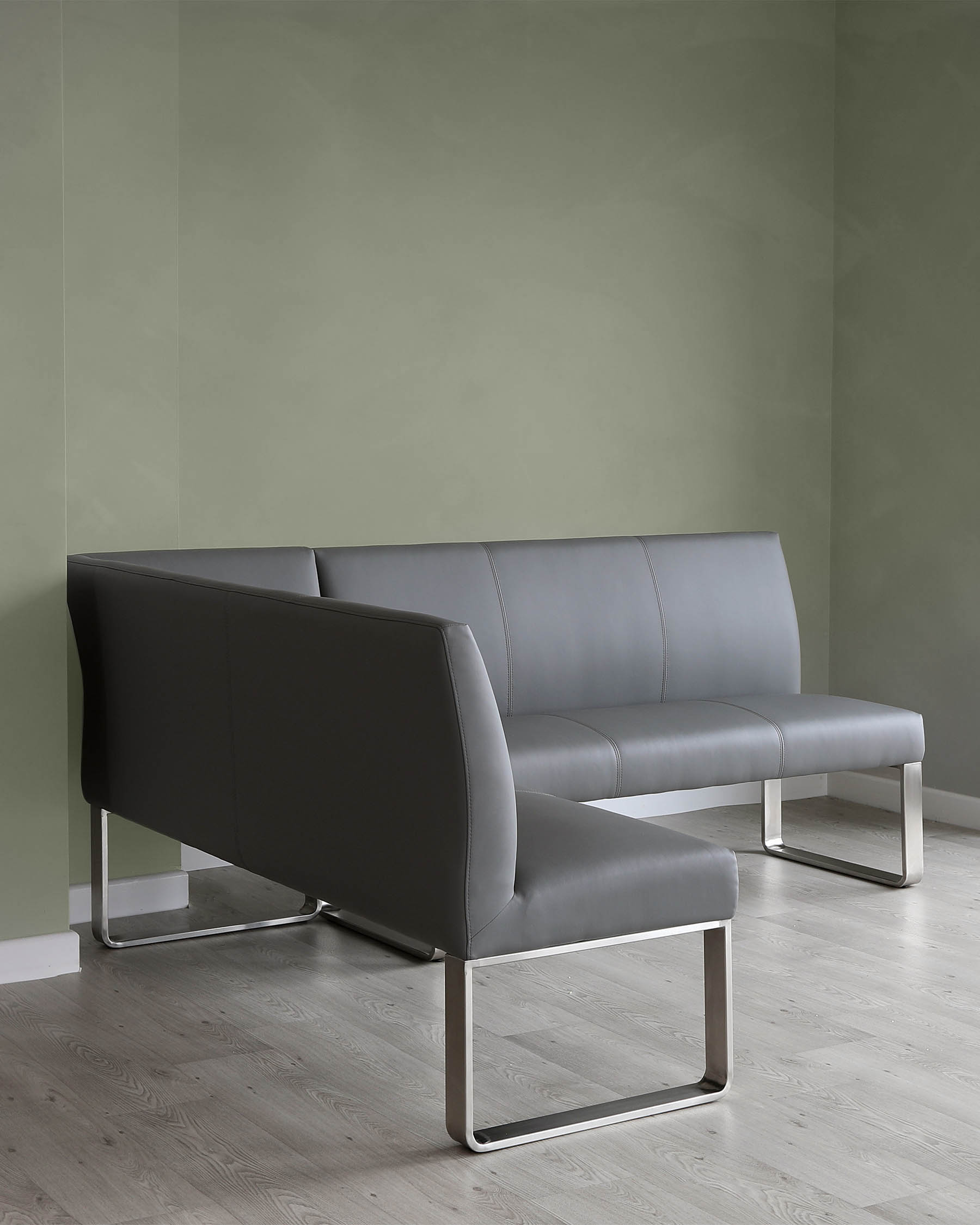 Modern charcoal grey leather sofa with a streamlined design, featuring a solid backrest, cushioned seating, and polished chrome cantilevered bases on a light wooden floor against a two-tone green wall.