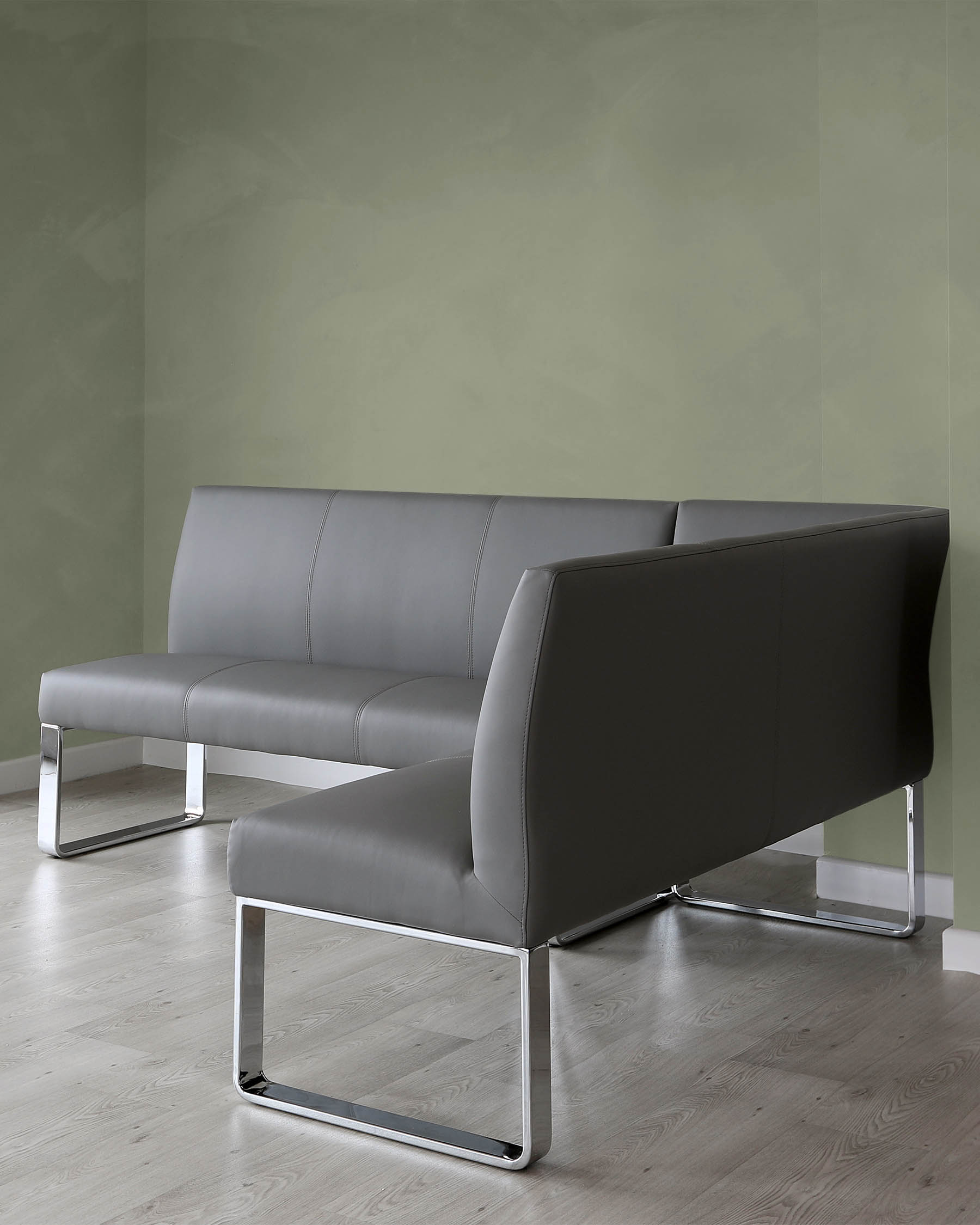 Modern minimalist-style grey leather sofa with sleek chrome metal legs, placed in an interior with muted green walls and light wooden flooring.