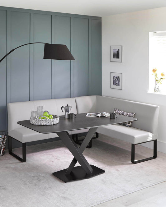 Modern dining nook featuring a rectangular, black dining table with a unique X-shaped base paired with a matching L-shaped bench upholstered in sleek grey leatherette.