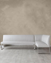 Modern minimalist L-shaped sectional sofa with white upholstery and sleek chrome legs, positioned in a room with light wooden flooring and a textured beige wall.