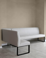 Modern minimalist white leather sofa with black metal frame support sitting on light wood flooring against a two-tone beige wall.