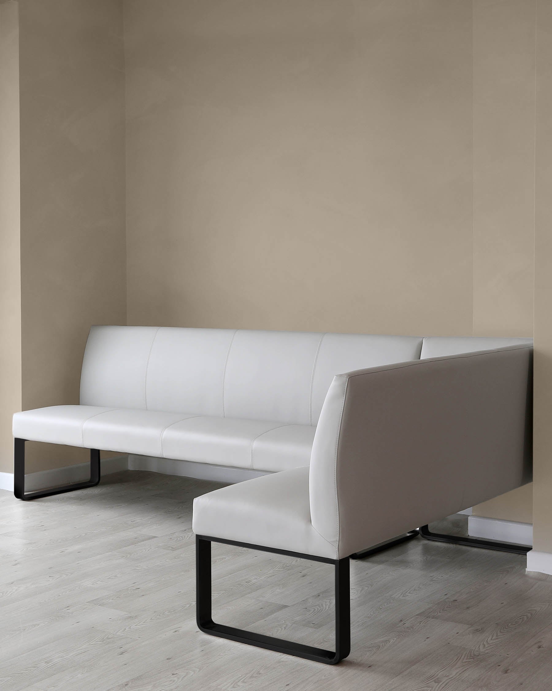 Minimalist white leather L-shaped sectional sofa with sleek black metal legs, displayed in a room with light wooden flooring and beige walls.