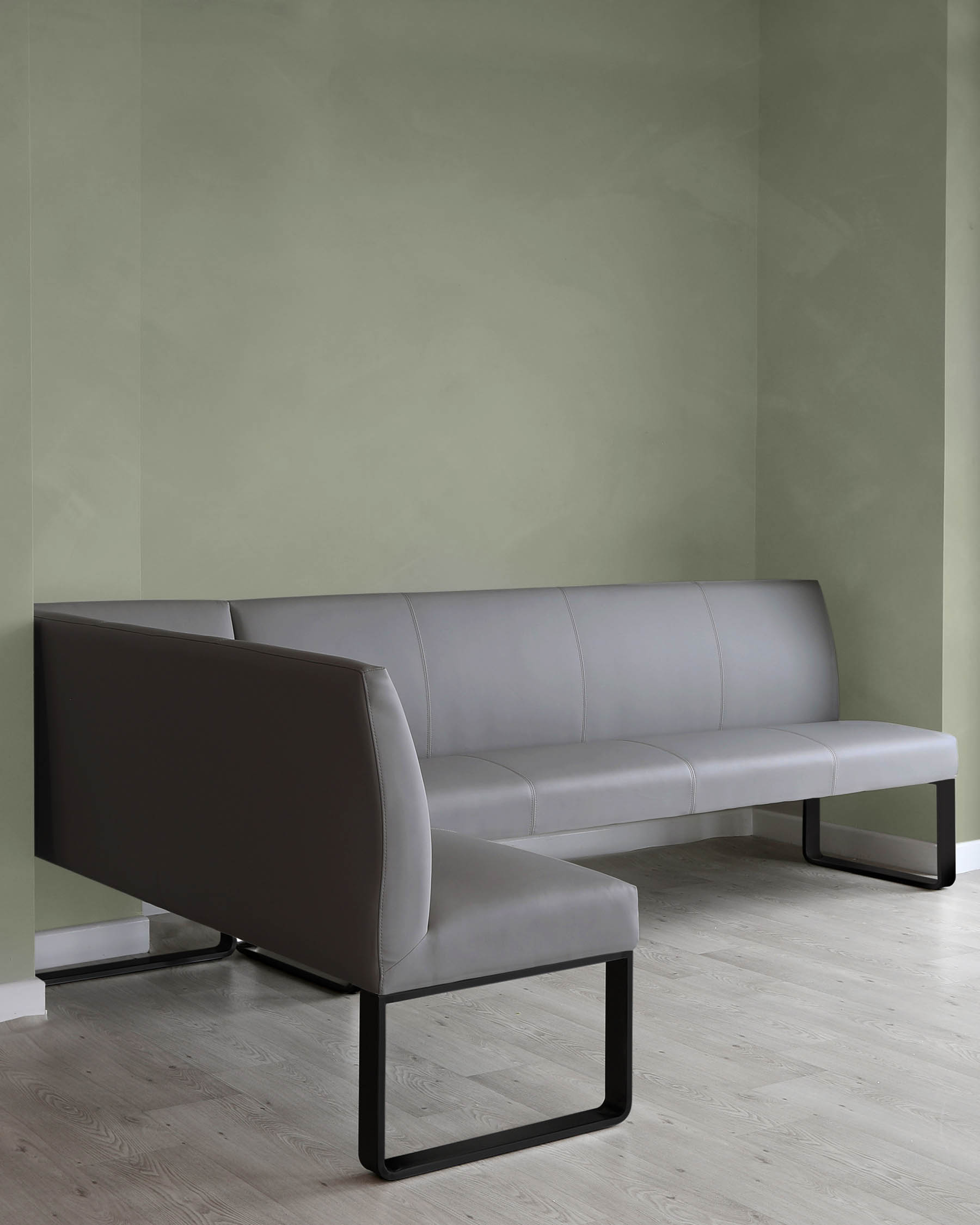 Modern minimalist grey upholstered bench sofa with a unique black metal base structure against a muted green wall on a light hardwood floor.