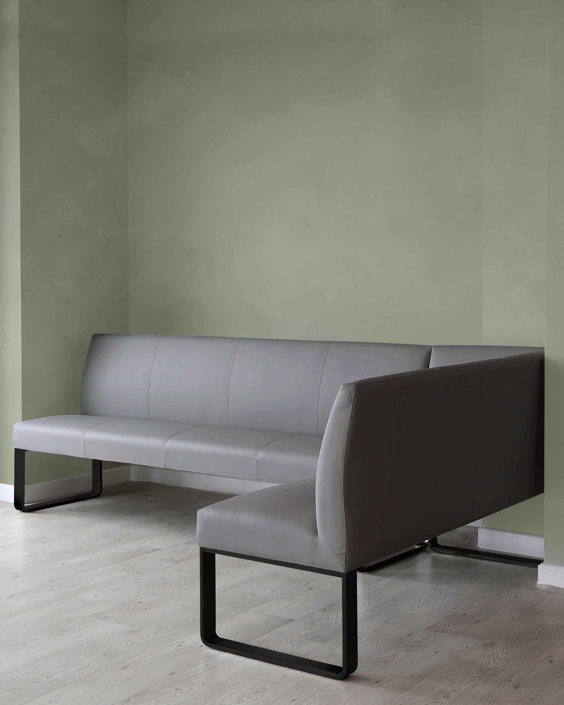 Modern L-shaped sectional sofa with a minimalist design, featuring grey upholstery and sleek black metal legs, situated against a muted green wall and light wood flooring.