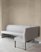 Modern light grey leather sofa with a minimalist design, featuring a low backrest and sleek, industrial-style metallic silver legs. The sofa has a continuous seat cushion and is set against a neutral backdrop with a light wood floor.