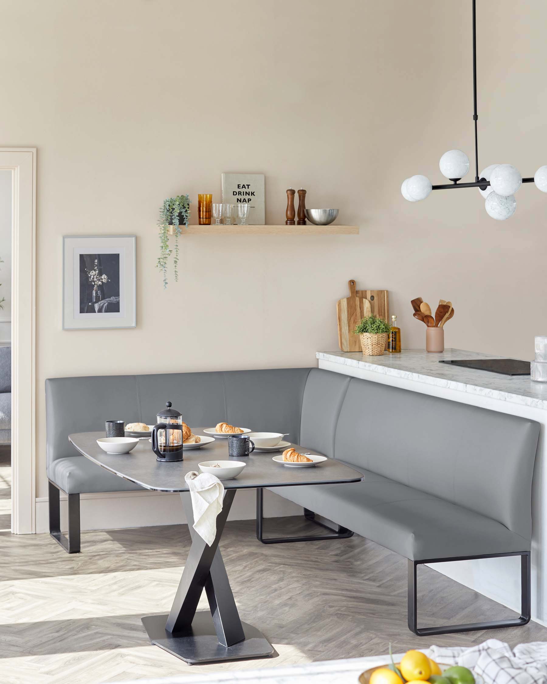 Modern dining space featuring a sleek, grey corner bench with a smooth finish, and a matching rectangular table with a unique black angular base design. Both pieces show a contemporary minimalist style.