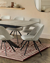 Modern dining table with a gray surface, surrounded by sleek, upholstered chairs, set on a patterned rug.