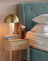 Elegant bedroom furniture featuring a plush, tufted, seafoam blue velvet headboard and a contemporary, pale wood bedside table with a single drawer and slender legs.