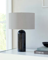 A sleek black lamp with a round base and neutral fabric shade sits beside stacked books on a white surface.