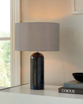 A sleek black marble lamp with a gray shade, accompanied by stacked books and a simple black bowl on a light-colored surface.