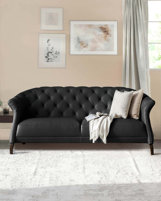 A stylish black tufted sofa with elegant curves, adorned with a soft throw blanket and accent pillows, set against a light wall.