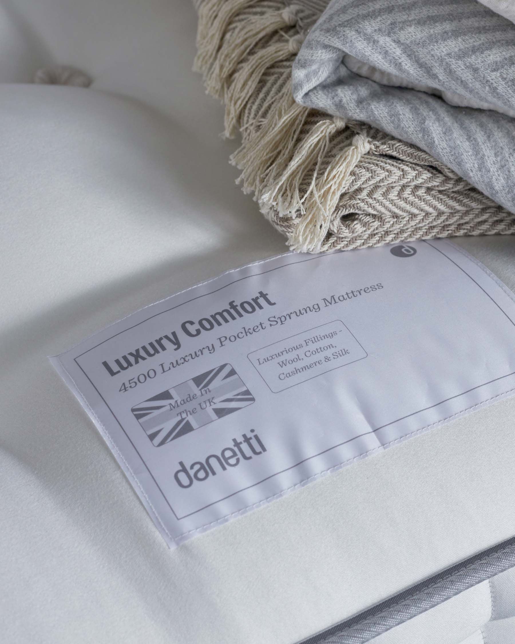 Luxury pocket sprung mattress with a tag detailing luxurious fillings, accompanied by soft layered blankets.