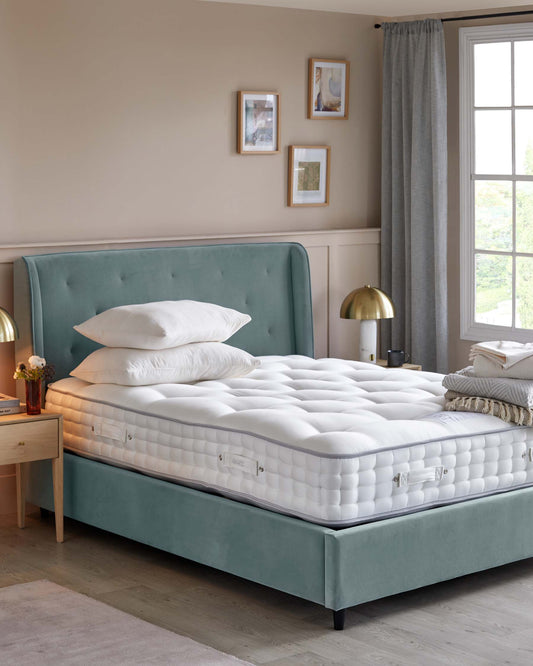 A teal upholstered bed frame with a tufted headboard, layered white mattress, and decorative pillows, paired with a wooden nightstand.