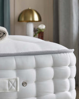 A plush white mattress with tufted detailing, accompanied by a stylish gold lamp and a small vase with flowers in the background.