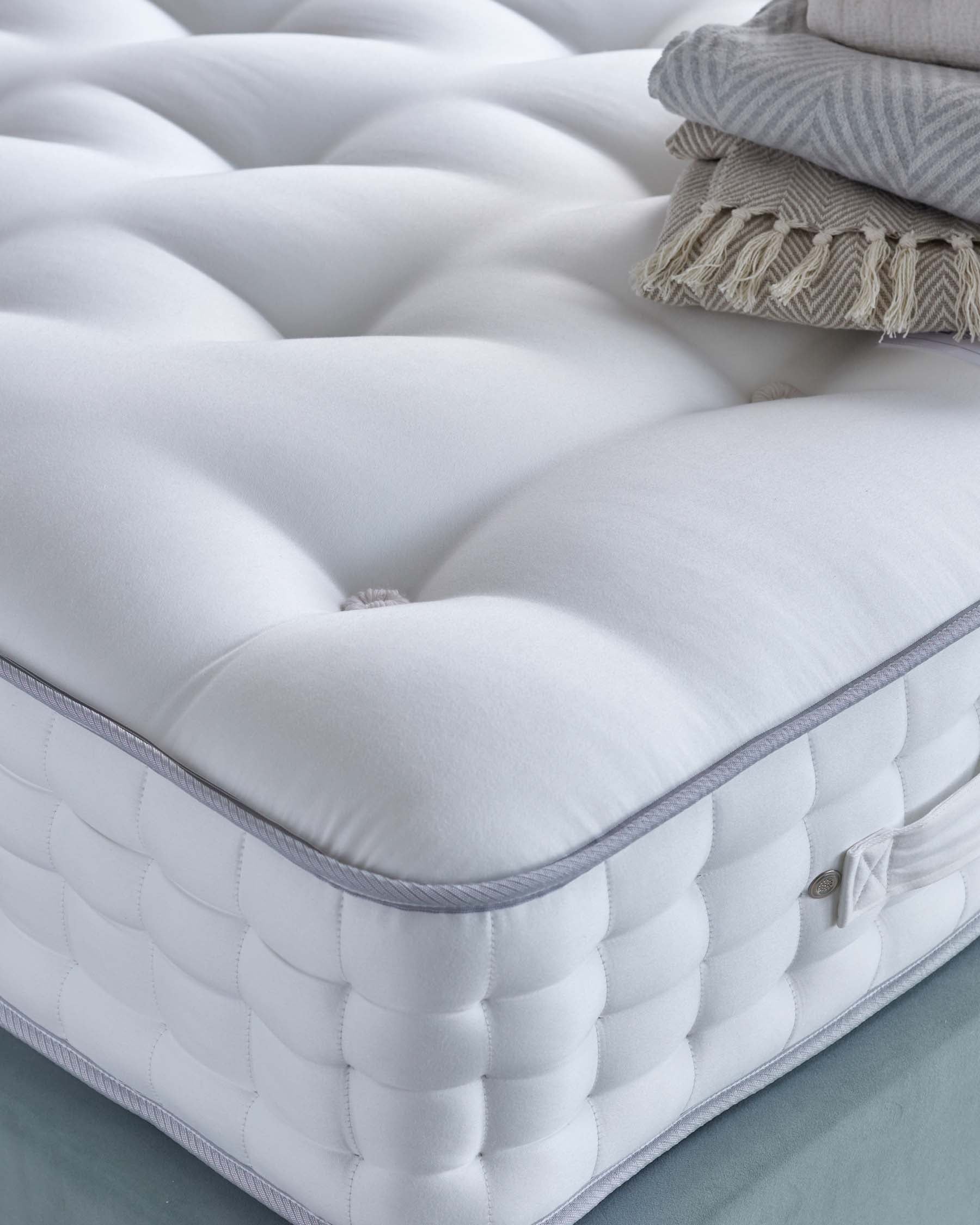 A plush, white mattress featuring tufted detailing, complemented by neatly stacked textured throws in soft, neutral tones.