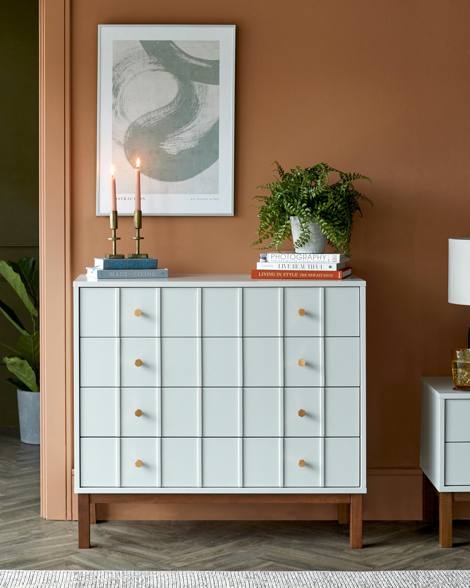 A light blue sideboard with golden knobs, complemented by candles, books, a potted plant, and a framed artwork against a brown wall.