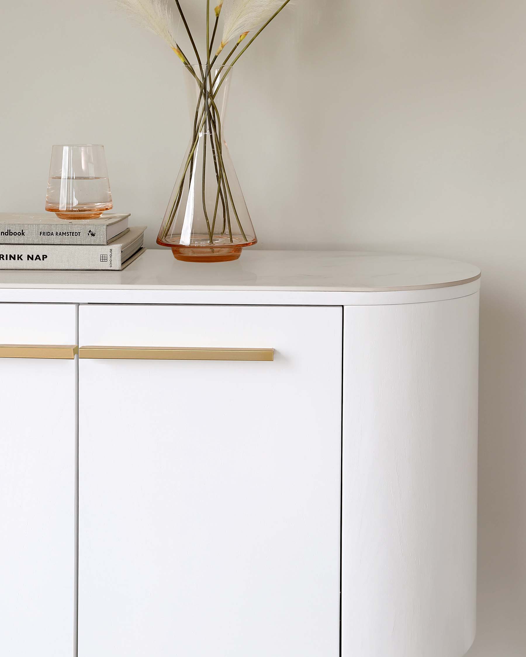 A modern white curved sideboard with minimalist design, featuring sleek built-in handles with a brass finish.