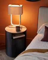 Modern cylindrical bedside table with vertical fluting and a white marble top, paired with an avant-garde table lamp featuring a rectangular fabric shade and a unique illuminated frame.