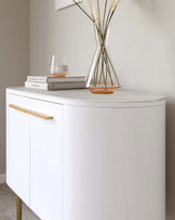 Elegant, modern white sideboard with sleek gold handles and curved contours, standing against a neutral-coloured wall.