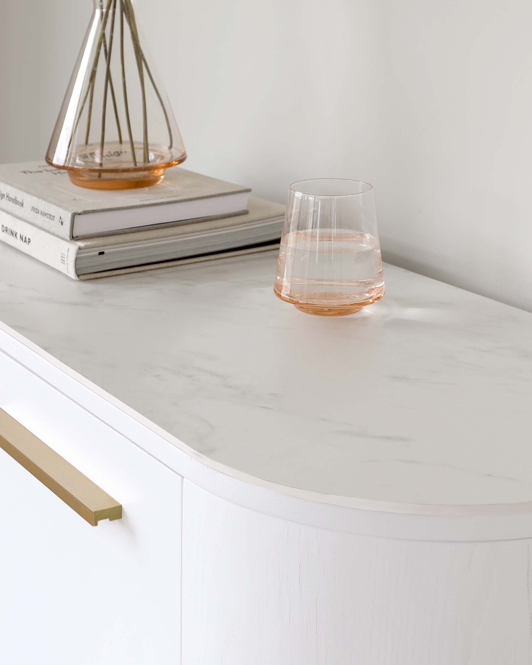 Elegant white console table with a curved front design, featuring a smooth marble-like tabletop and brass handle accents.