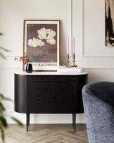 Elegant mid-century modern style sideboard with a curved silhouette, featuring a textured wood grain finish in black. The sideboard is supported by slender tapered legs and offers cabinet storage, showcased in a contemporary living space. A portion of a textured fabric armchair with dark and light blue hues is visible to the right.