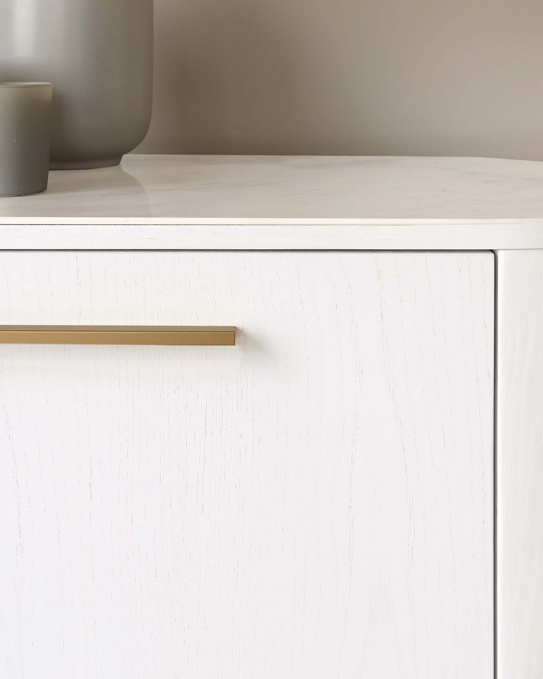 Contemporary white textured cabinet with a minimalist gold handle, featuring a smooth faux marble top, partially obscured by two cylindrical grey vases.