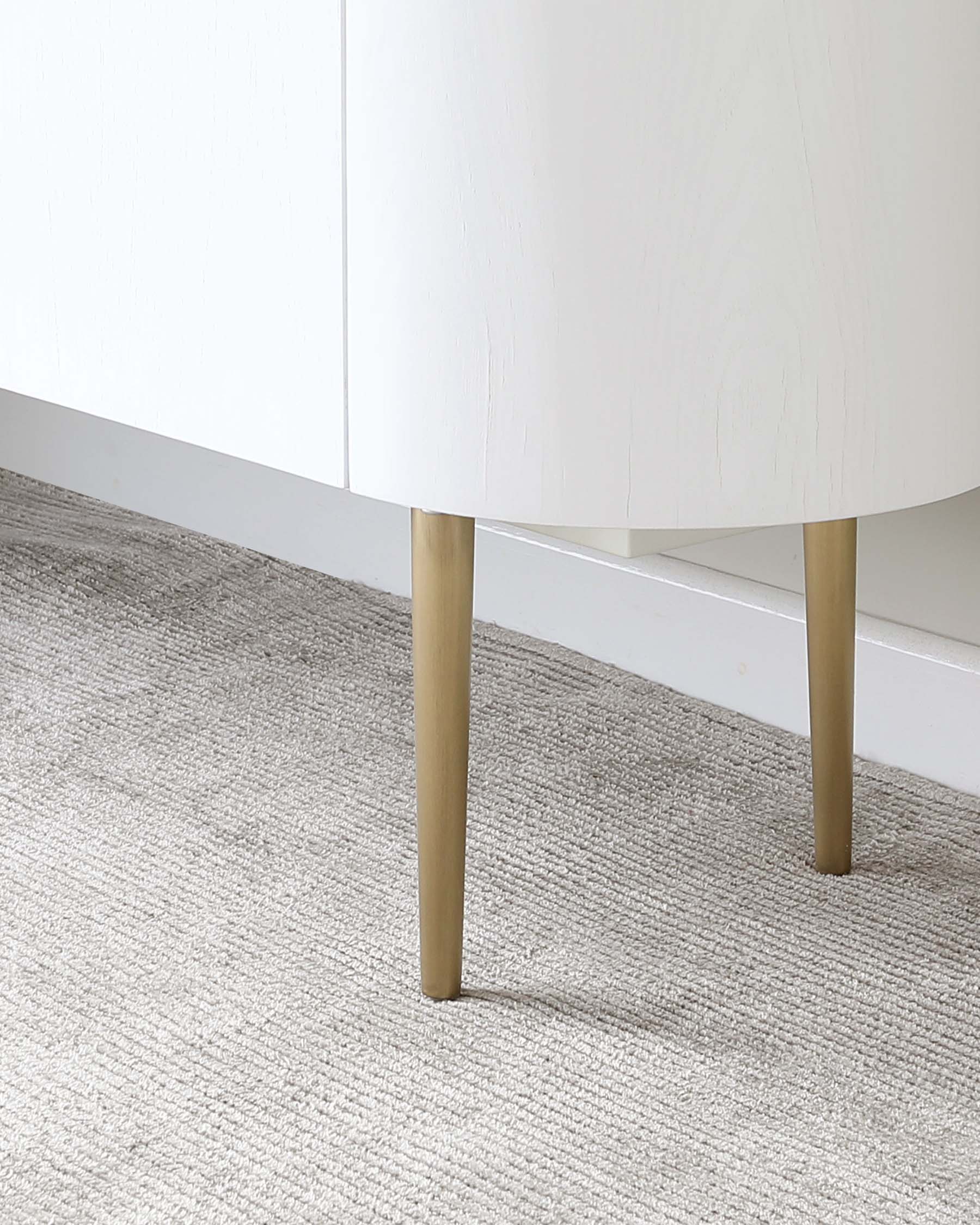 Modern minimalist white cabinet with round edges and natural wood tapered legs, standing on a textured grey carpet.