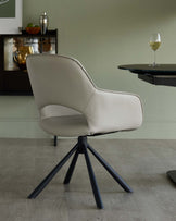 Modern beige chair with a curved backrest and black tripod legs, paired with a sleek glass-top table, set in a minimalist space.