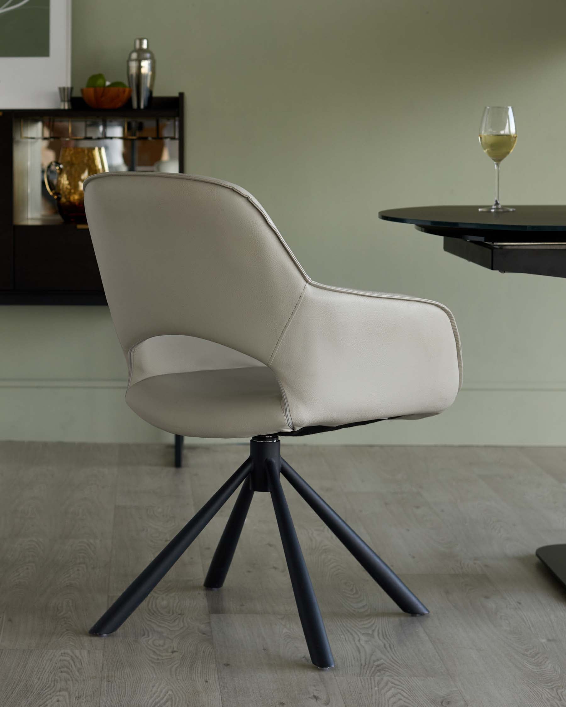 Modern beige chair with a curved backrest and black tripod legs, paired with a sleek glass-top table, set in a minimalist space.