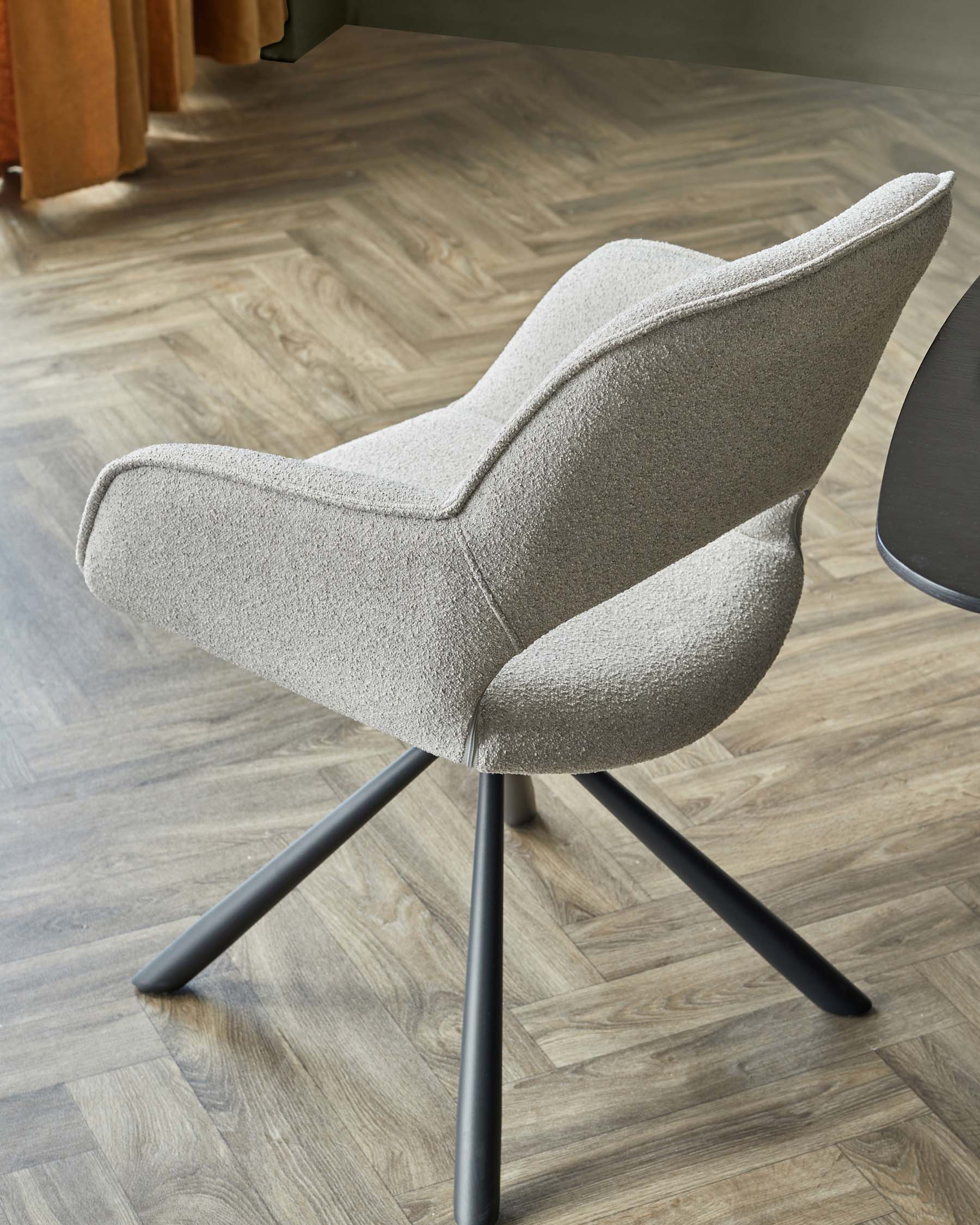 Modern light grey textured fabric armchair with streamlined wingback design and black metal swivel base, showcased on a herringbone parquet floor.