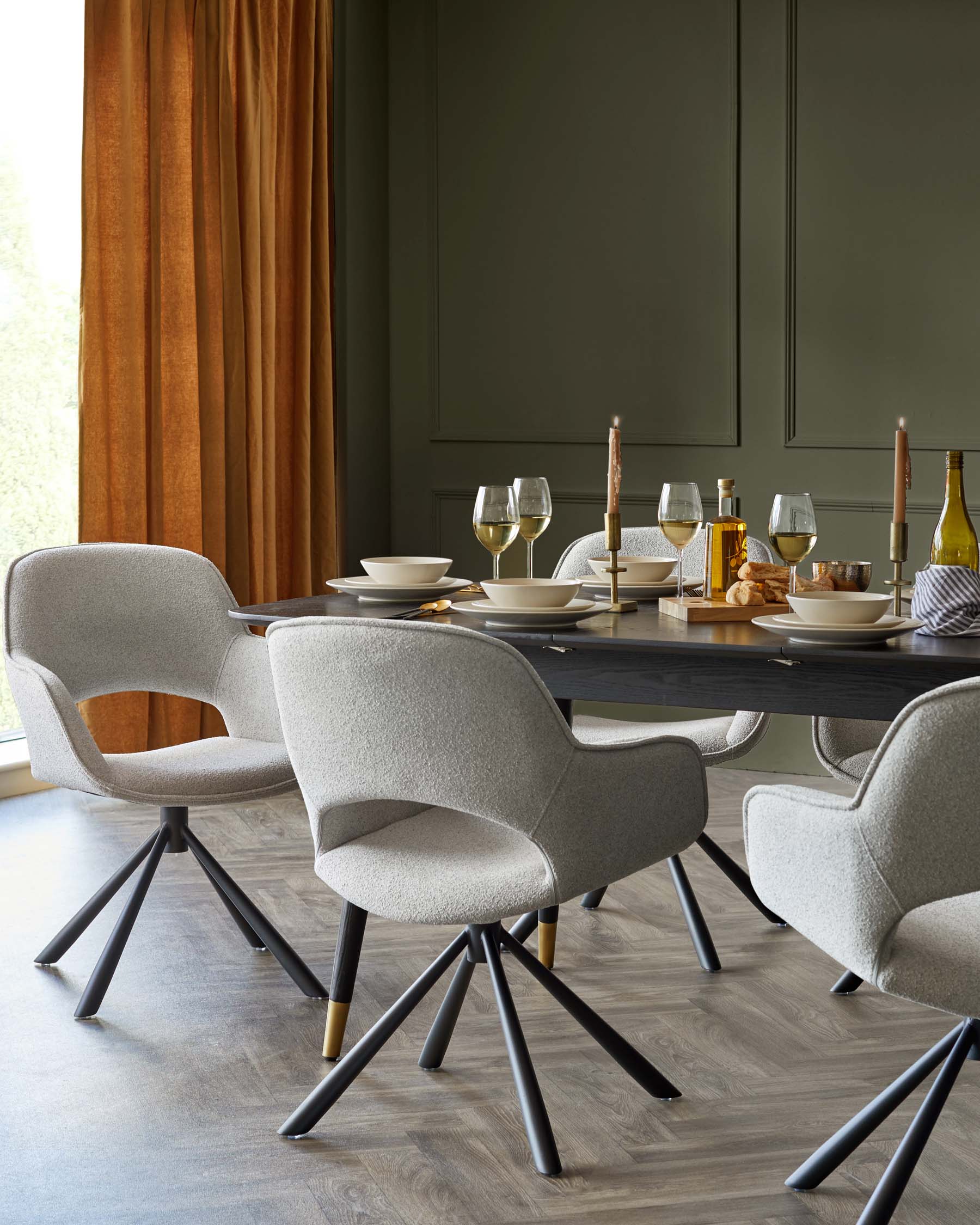 Modern dining room featuring an elegant rectangular dark wood table surrounded by four light grey upholstered chairs with unique black metal legs accented with gold tips. The table is set with white plates, wine glasses, and a mixture of decorative and functional tableware, creating a sophisticated dining setup.