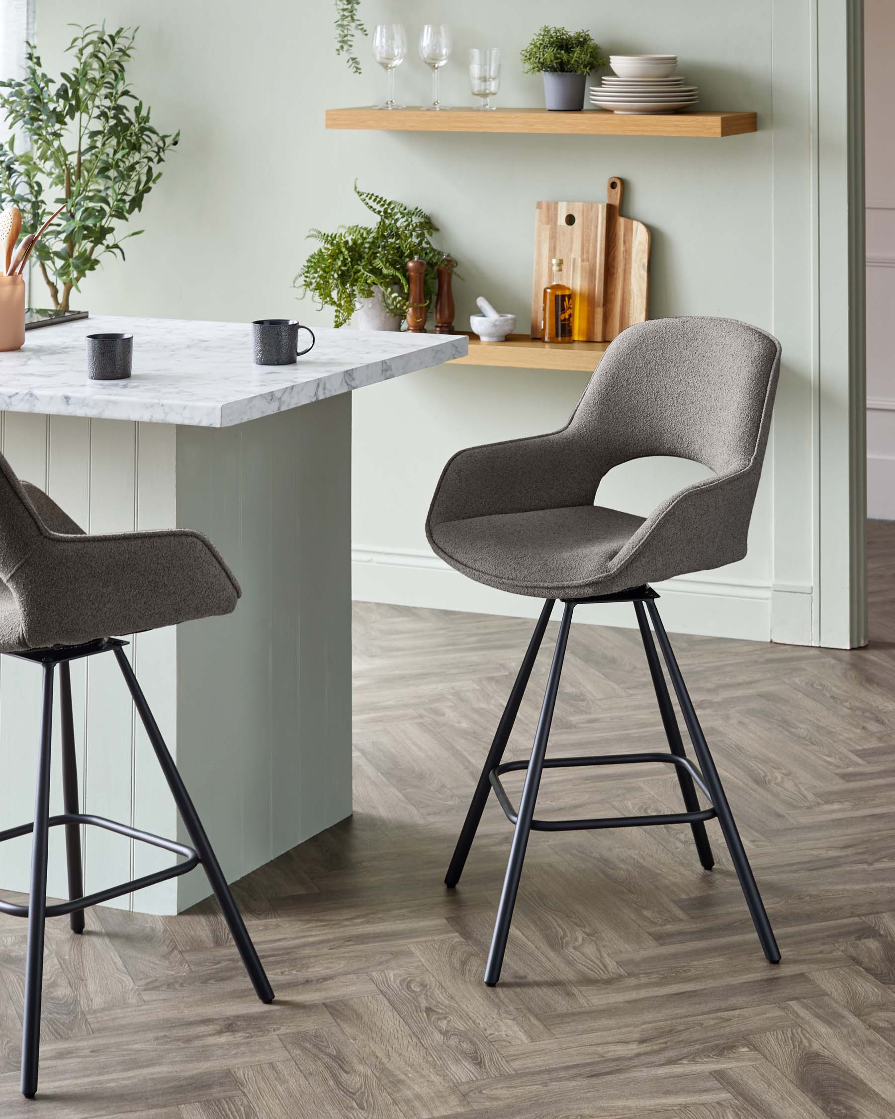 Elegant modern grey fabric bar chairs with comfortable curved backrests and slender black metal legs, positioned near a kitchen island with a marble countertop.