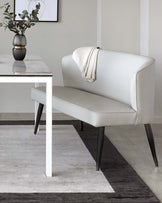 Sleek white upholstered bench with black legs beside a modern marble-top table, accented by a decorative vase and a cozy throw.